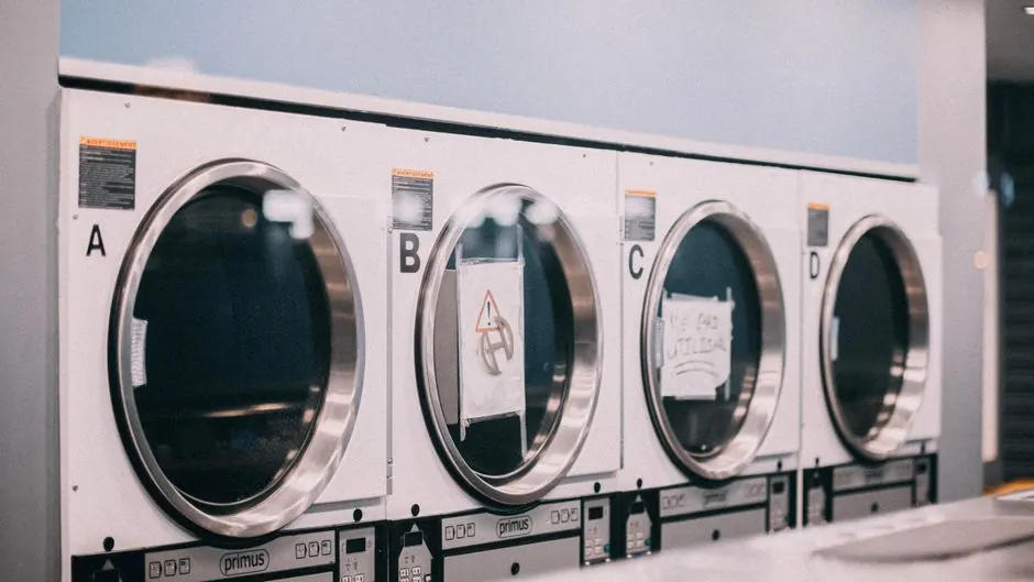 A series of industrial washing machines in a modern laundromat setting.